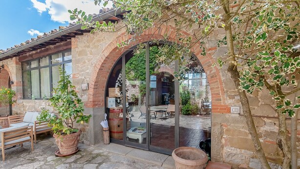A rustic building with a stone facade, a glass door entrance, and a patio area with outdoor seating. - Villa Vigneto Estate (Gaiole in Chianti)