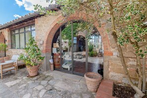 Un bâtiment de style rustique, doté d’une façade en pierre, d’une porte d’entrée en verre et d’un patio aménagé avec des sièges extérieurs.
