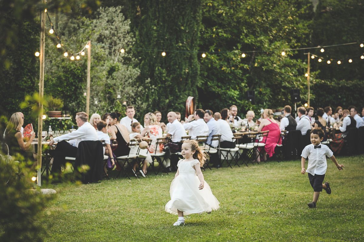 A grassy outdoor area with string lights and people seated at tables.