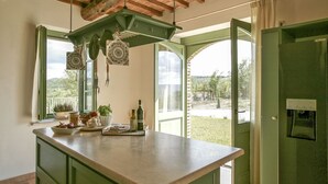 Una cocina con una isla grande, armarios verdes, utensilios de cocina colgantes y vistas al exterior.