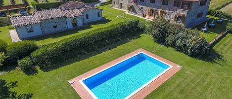 Una amplia casa de piedra con piscina, rodeada de césped cuidado y una cancha de tenis.
