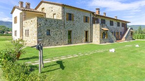 A stone building with a large lawn and a staircase leading to a second floor.