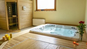A sauna room with a wooden floor, a large hot tub, and a glass-enclosed sauna.
