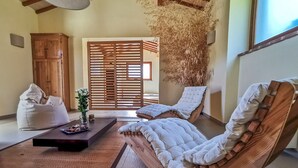 A room with a wooden sofa, a bean bag, a small table with a vase and a plate, and a wooden partition with a window.