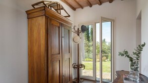 Um armário de madeira com um porta-chapéus, uma porta de vidro que dá para um jardim, e uma mesa com um vaso.