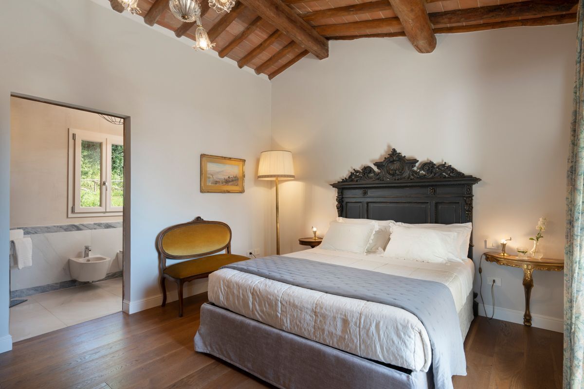 A bedroom with a bed, bedside table, lamp, and a chair.