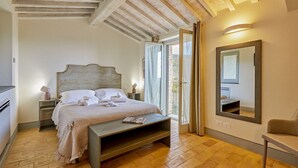 Een slaapkamer met een houten bed, nachtkastjes, een bankje, een grote spiegel en een schuifglazen deur naar buiten.