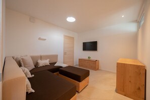 A modern living room with a sectional sofa, a wooden cabinet, and a flat-screen TV mounted on the wall.