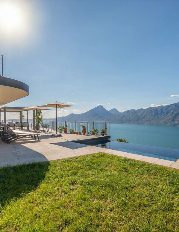 Une terrasse dotée de mobilier d’extérieur et d ’une piscine, offrant une vue sur un lac avec des montagnes en arrière-plan.