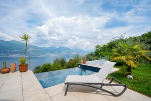 Un espace aménagé au bord de la piscine, avec un fauteuil de relaxation, des plantes en pot et une vue sur un lac et des montagnes.
