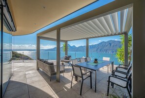 Un espace extérieur aménagé, abrité et doté d’une table et de chaises, offrant une vue panoramique sur les montagnes et le lac.