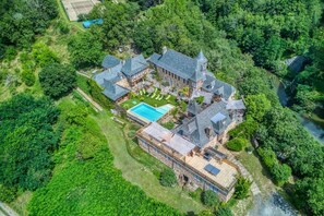 An aerial view of a large, stone-built estate with multiple buildings, a swimming pool, and lush greenery surrounding the property.