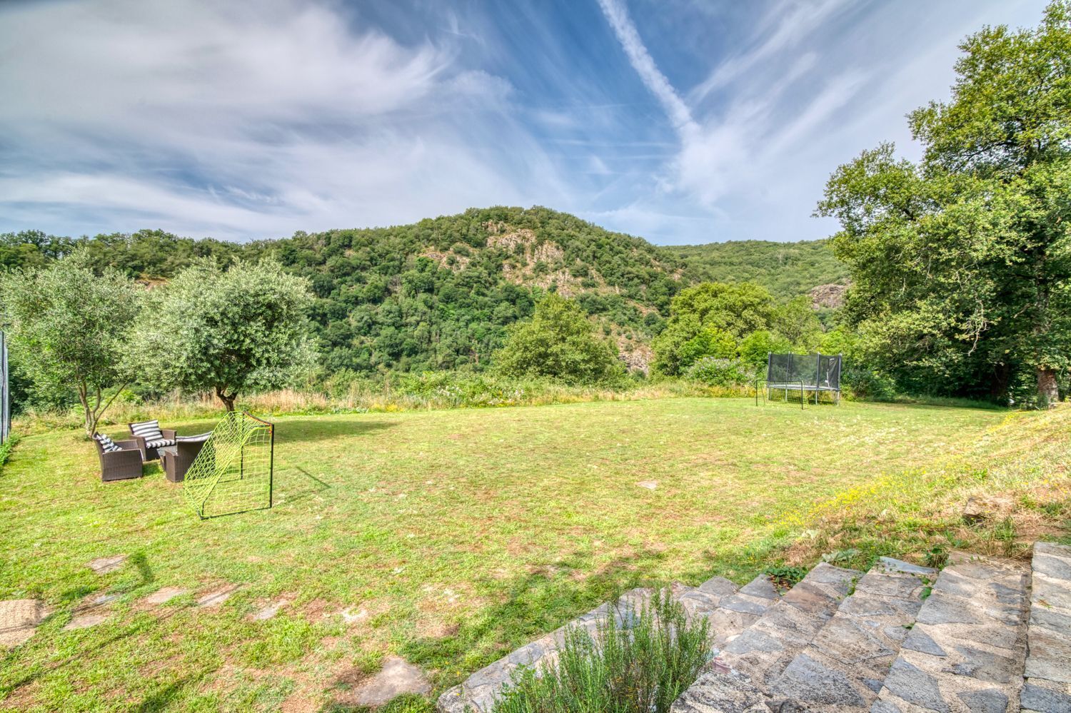 A grassy outdoor area with a stone pathway, a swing set, and a seating area with chairs.
