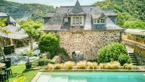 Una casa de piedra con piscina, rodeada de exuberante vegetación y colinas.