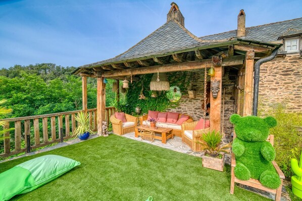 A covered patio with wicker furniture, a green lawn, and a stone building in the background.