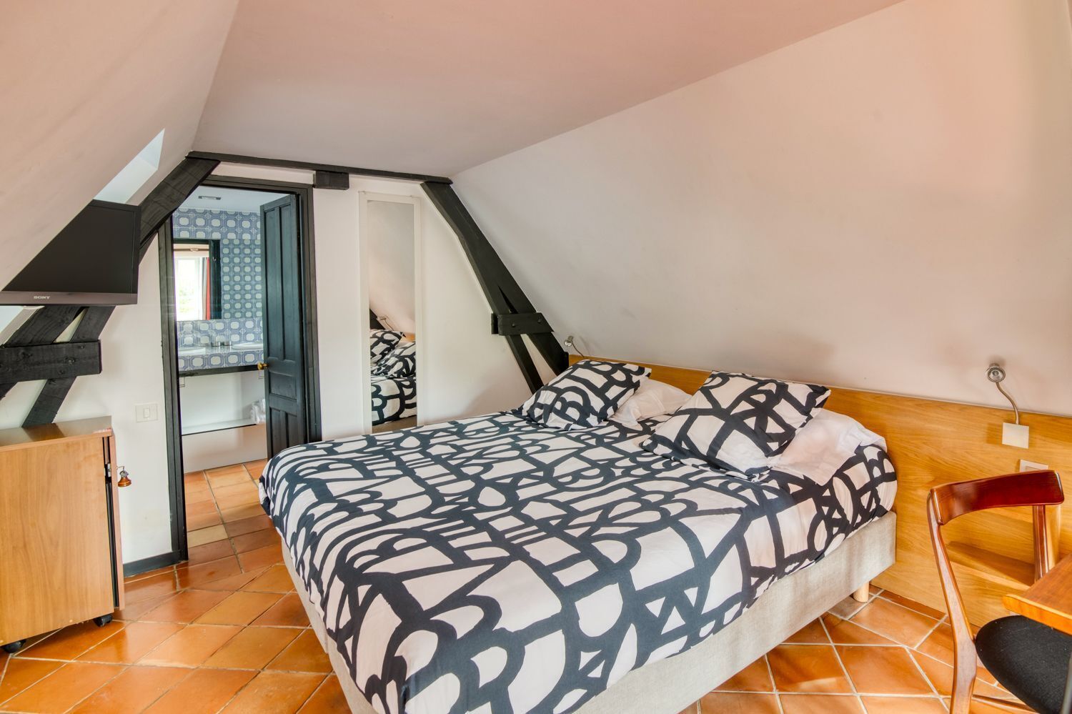 A bedroom with a bed, a wooden dresser, a chair, and a staircase leading to an upper room.