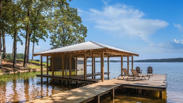 A wooden dock extending into a calm lake, with a covered seating area and lounge chairs.