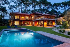 Una casa de madera de dos pisos con piscina, rodeada de árboles.