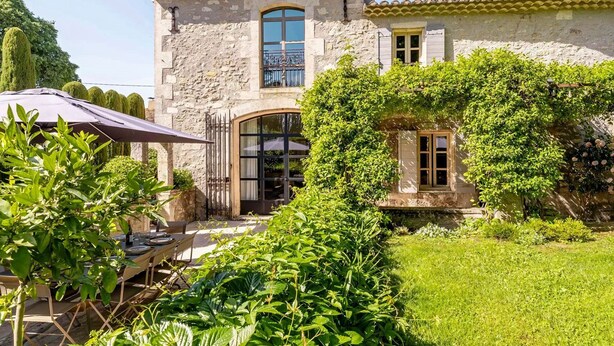 A stone building with a tiled roof, a large arched doorway, and a covered patio area with outdoor furniture.