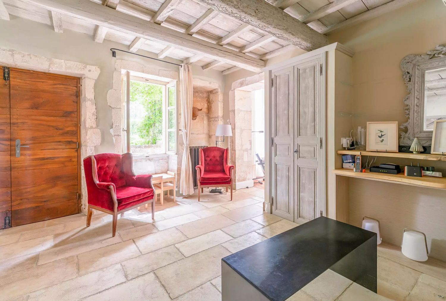 A room with a wooden door, red upholstered chairs, a black table, and a white door with a mirror.
