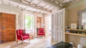 A room with a wooden door, red upholstered chairs, a black table, and a white door with a mirror.