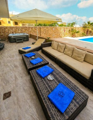 Een zwembadgedeelte met een stenen muur, een loungesofa en een jacuzzi.
