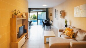 Een moderne woonkamer met een televisie, bank, salontafel en een eethoek met stoelen en een tafel.