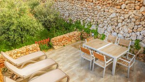 Een terras buiten met een stenen muur, een houten tafel met stoelen en loungestoelen.