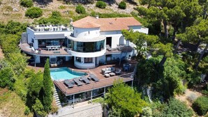 Una villa moderna con piscina, mobiliario exterior y vistas panorámicas a una colina.