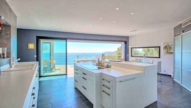 Cocina moderna con una isla grande, vista al mar y puerta corrediza de vidrio que da a un balcón.