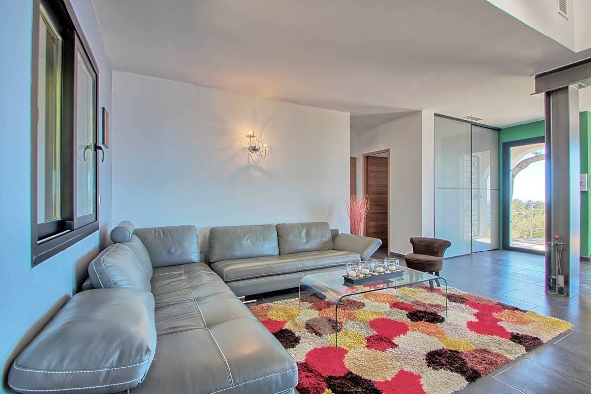 A modern living room with a grey sectional sofa, a glass coffee table, and a colorful rug.