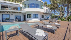Una villa moderna con piscina, tumbonas y una estructura circular de vidrio.