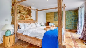 A four-poster bed with a stone wall backdrop, a wooden headboard, and a blue throw blanket.
