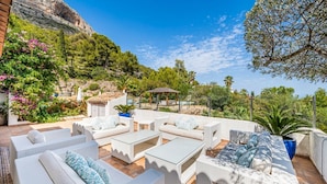 An outdoor patio with wicker furniture, a pergola, and a view of a mountainous landscape.