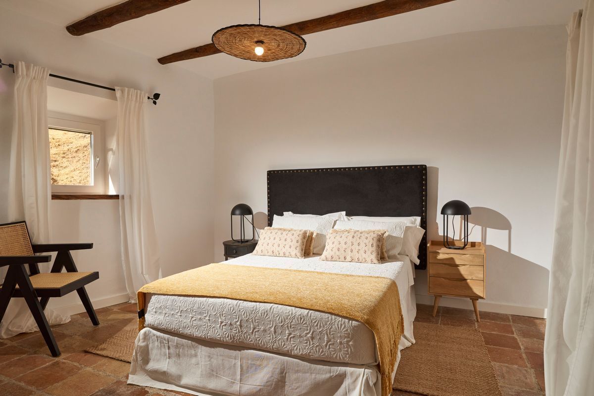 Une chambre à coucher avec un grand lit, deux tables de chevet avec des lampes, une chaise et une fenêtre avec des rideaux.