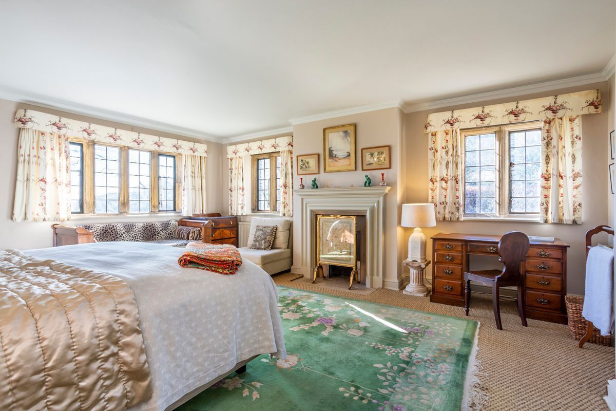 A bedroom with a large bed, a desk, a chair, a fireplace, and floral curtains.