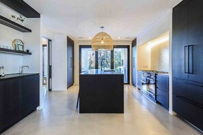 Une cuisine moderne dotée d’un îlot central, de meubles de couleur sombre et d’un luminaire suspendu.