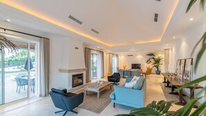 A spacious living room with a fireplace, a dining area, and a kitchen in the background. - Villa Mingo - Five Bedroom Villa, Sleeps 10 (Almansil)