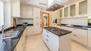 A modern kitchen with white cabinetry, a central island, and a built-in stove. - Villa Mingo - Five Bedroom Villa, Sleeps 10 (Almansil)
