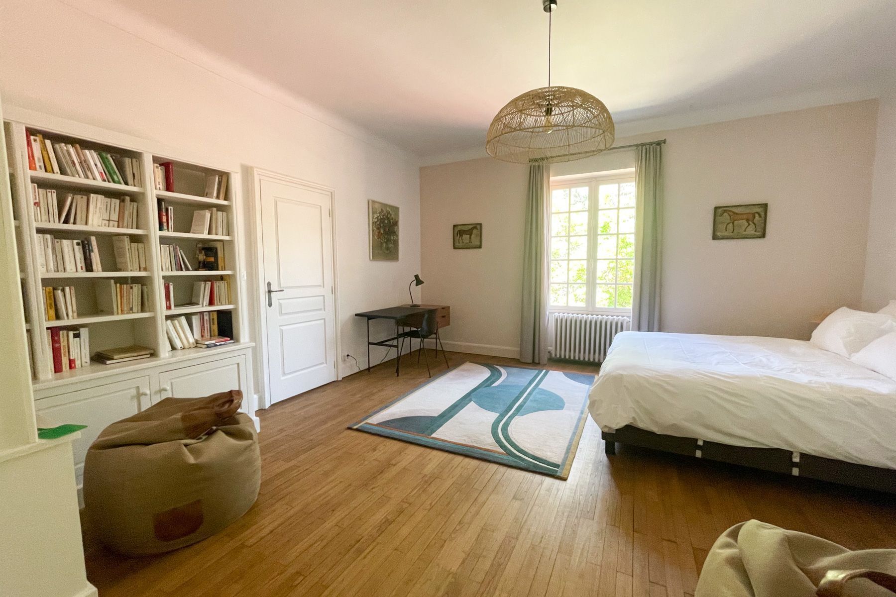 Une chambre à coucher avec un lit, une bibliothèque, un bureau, une chaise et une fenêtre avec des rideaux.