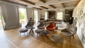 A spacious living room with wooden flooring, a large sofa, multiple armchairs, and a bookshelf. - Domaine Des Maronniers (Carsac-Aillac)