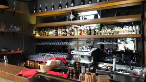 Zona de bar con estantes llenos de botellas, copas y una vitrina con alimentos.