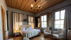 Un dormitorio amplio con una cama grande, dos sillones, techo de madera y ventanas grandes.