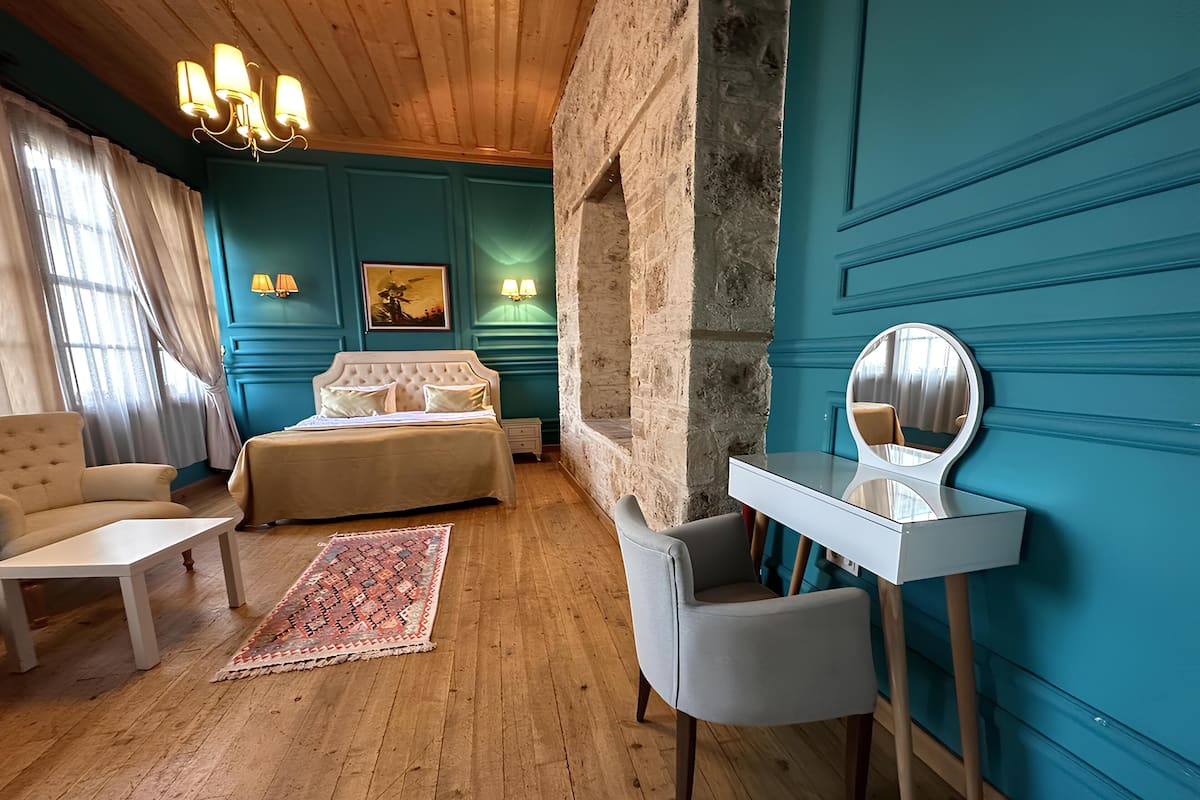 A bedroom with a bed, a desk, a chair, a rug, and a mirror.