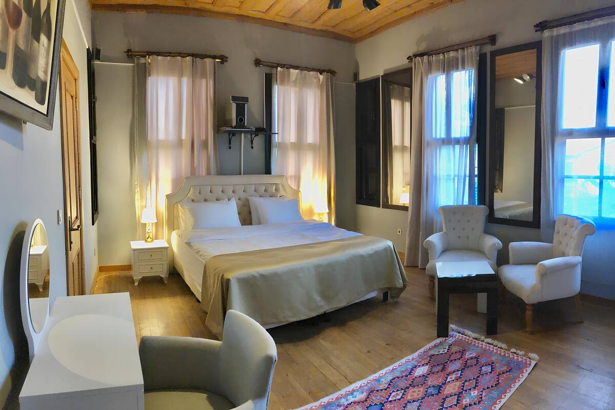 A bedroom with a large bed, two bedside tables, a chair, a desk, and a rug.