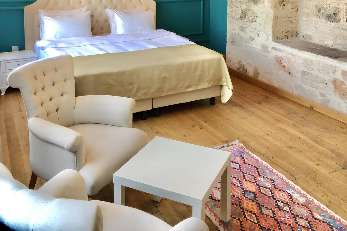 A bedroom with a bed, a chair, a small table, and a fireplace.