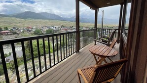 Una terraza de madera con una mesa y sillas, con vistas a un río y un pueblo con montañas al fondo.