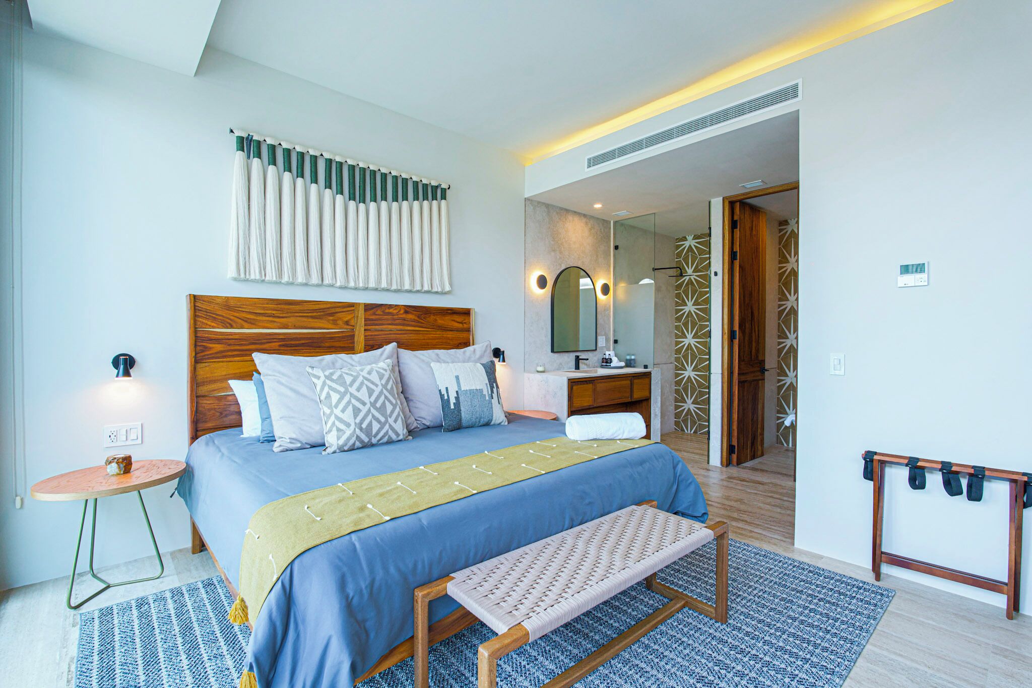 A modern hotel room with a large bed, bedside table, and a bench.