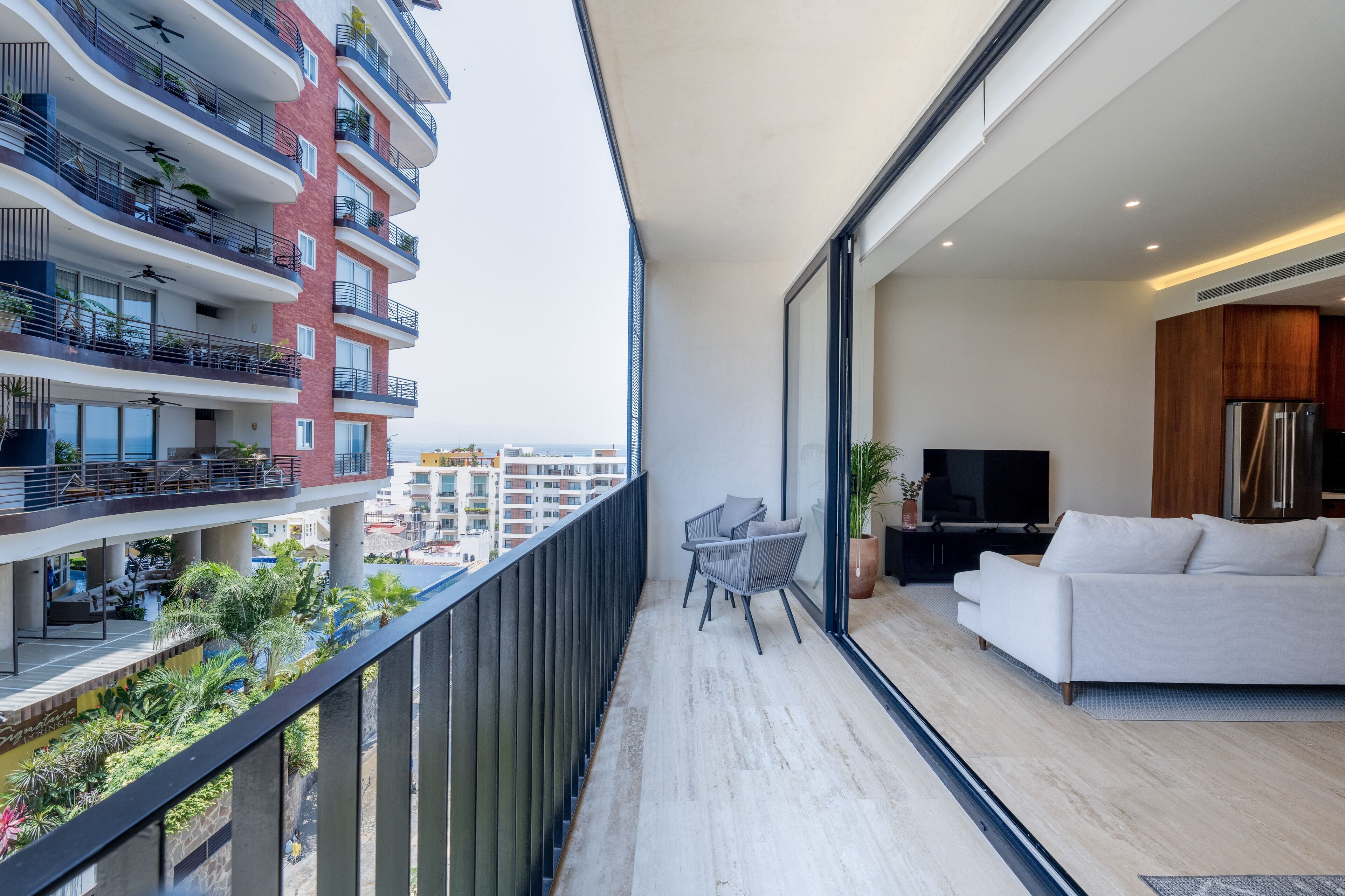 A modern apartment with a balcony, a white sofa, a TV, and a dining area.