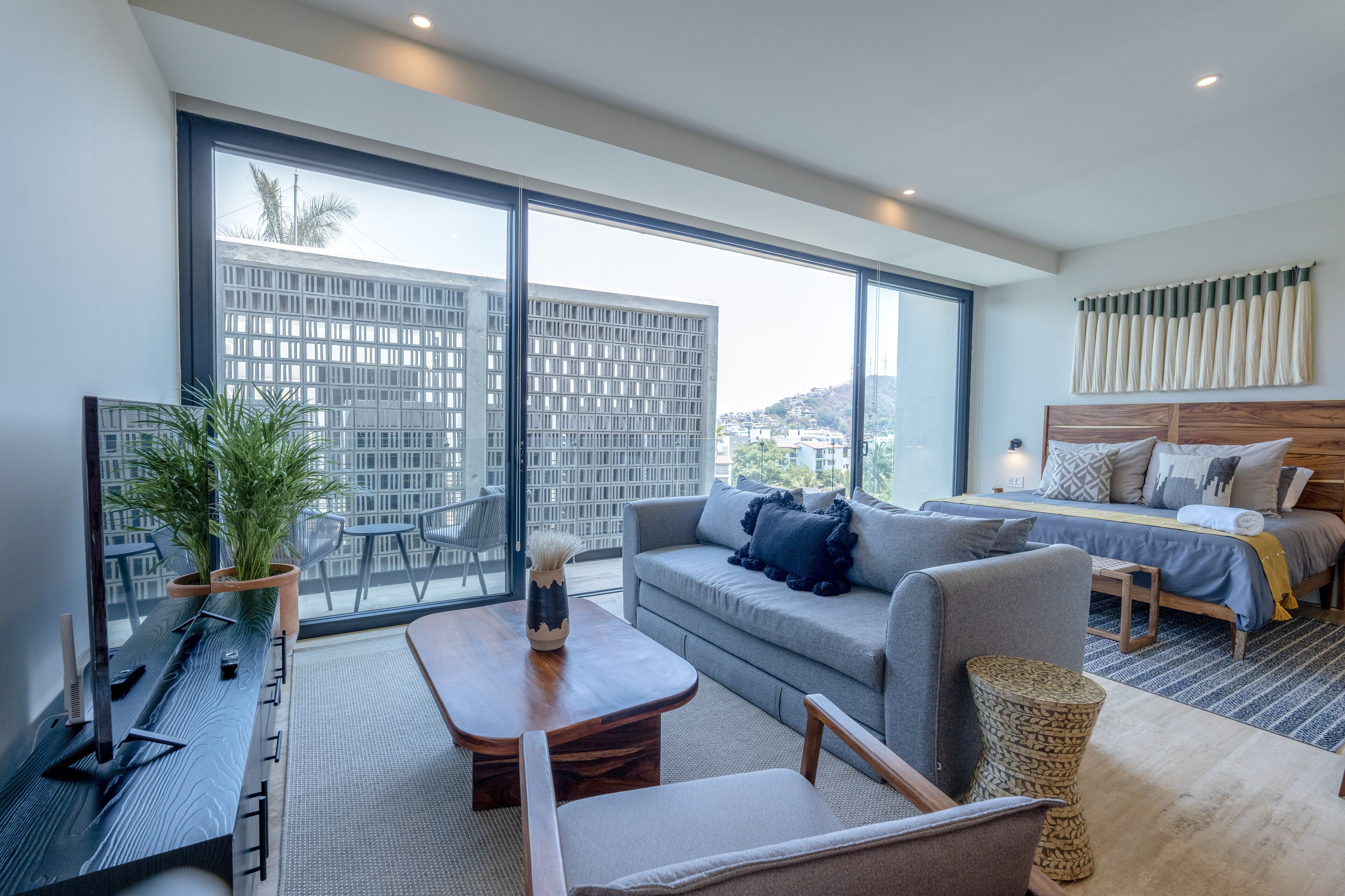 A modern hotel room with a large balcony, a sofa, a bed, and a dining area.